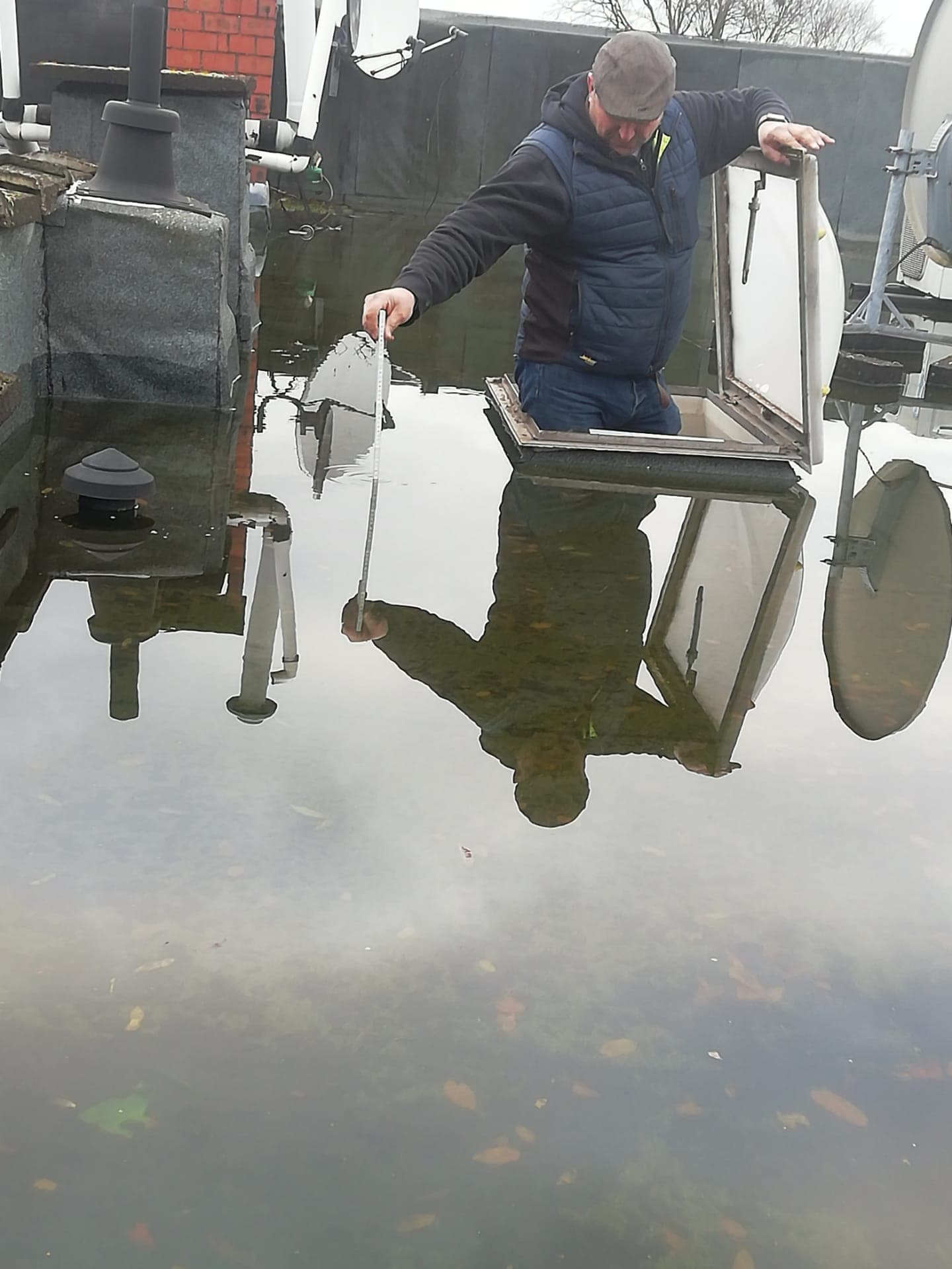Dakwerker controleert waterstand en afvoer op plat dak tijdens onderhoud