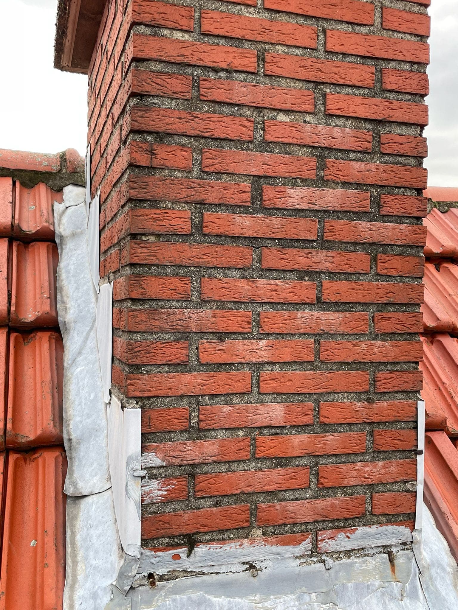 Schoorsteen met nieuw loodwerk en hersteld voegwerk aan de basis